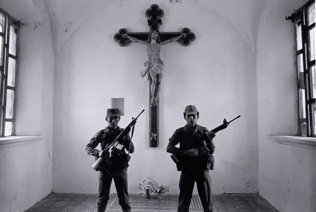 Black-and-white photograph of two armed soldiers standing symmetrically inside a church beneath a large crucifix.